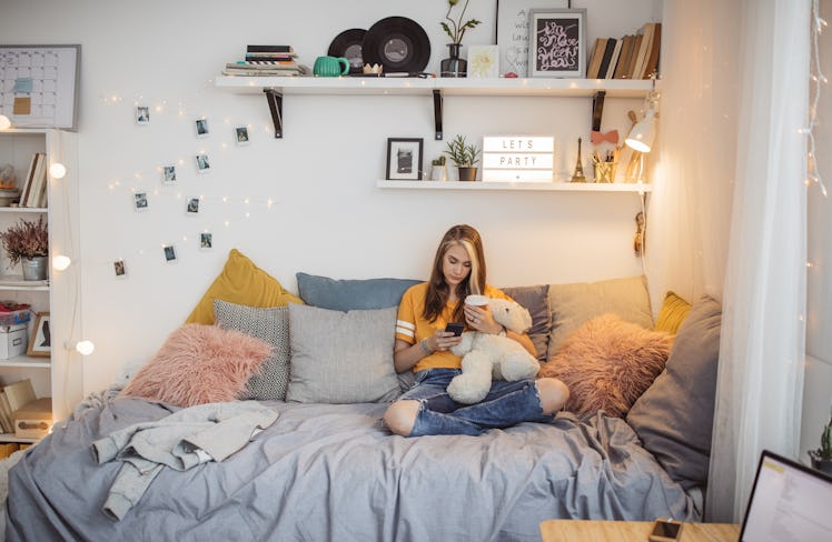 A trendy teen sits in her bedroom that's decorated in cool decor and texts.