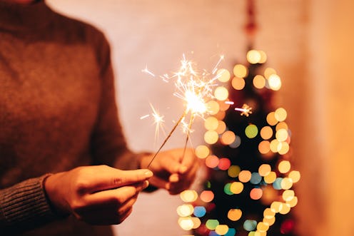 A woman holds up sparklers in front of a lit christmas tree. This year, celebrate new year's eve saf...