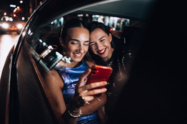 Two young women sit in a car at night and look at a phone while experiencing a drive-thru Christmas ...