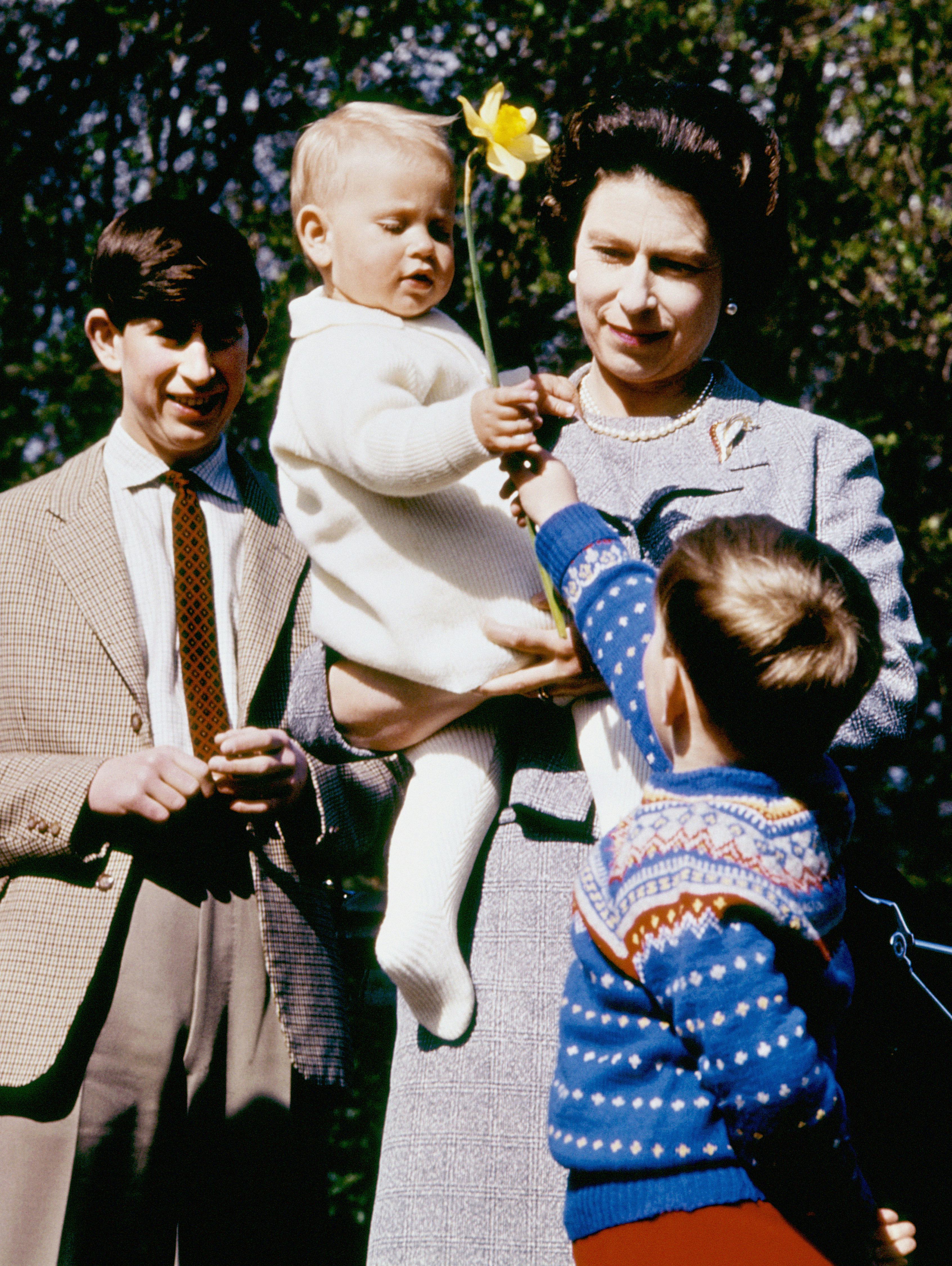 Queen Elizabeth the second holding a baby while standing next to Prince Charles and a child