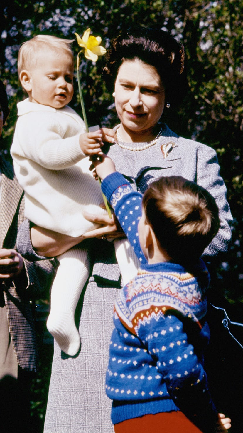 Queen Elizabeth the second holding a baby while standing next to Prince Charles and a child