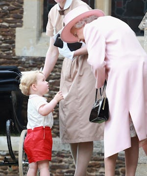 Queen Elizabeth II in a pink coat and hat leaning slightly toward a toddler