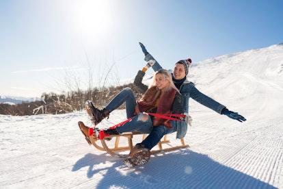 A man and woman sled down a slope, spreading their hands out as if flying down the hill. 