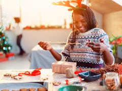 A woman in reindeer antlers decorates her Christmas gift using ribbons and string