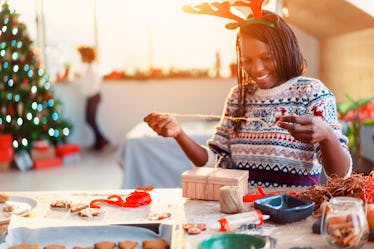 A woman in reindeer antlers decorates her Christmas gift using ribbons and string