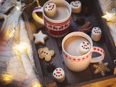 Two mugs of hot chocolate with snowman marshmallows are placed on a festive tray.