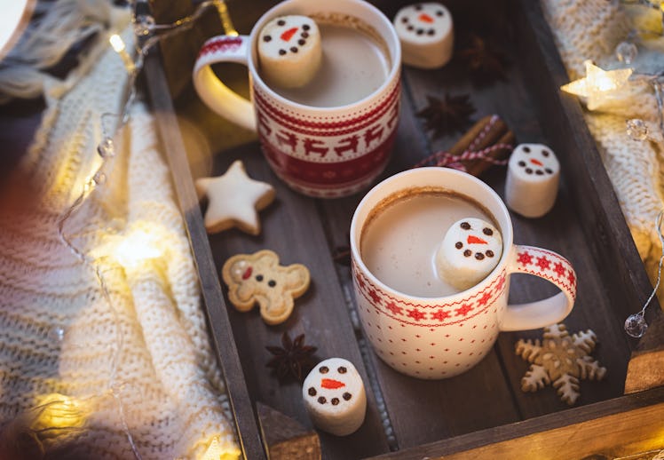 Two mugs of hot chocolate with snowman marshmallows are placed on a festive tray.