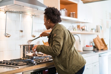 A young Black woman checks and stirs a pot of homemade soup on a snow day.
