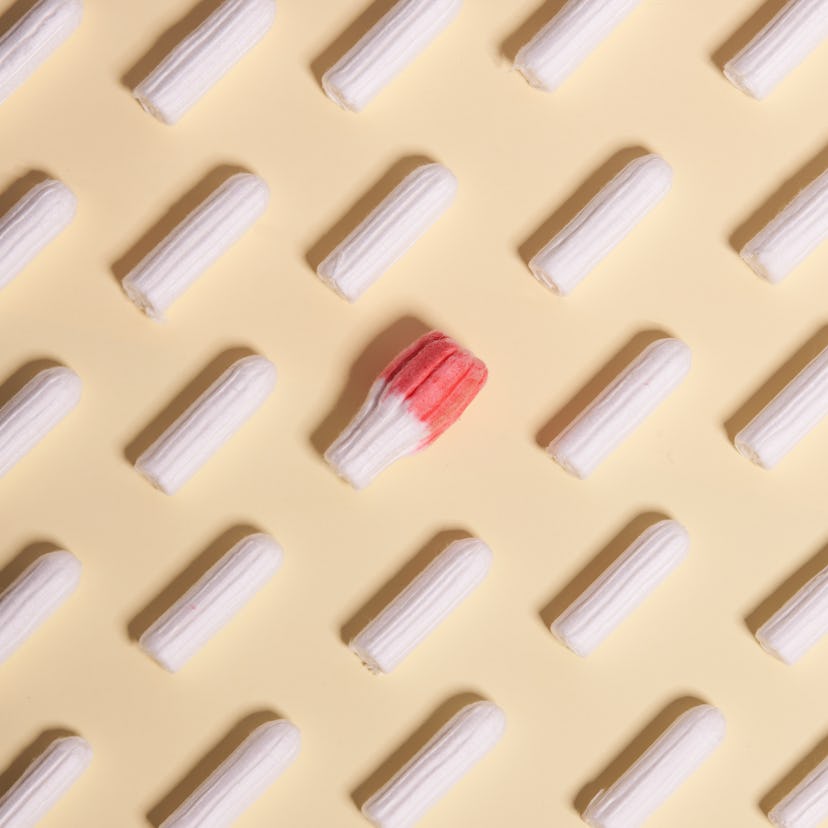 Tampons on a yellow background with one red expanded tampon. Having COVID-19 can affect periods, peo...