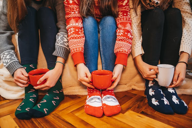 Three women wearing Christmas socks hold their festive mugs of hot chocolate.