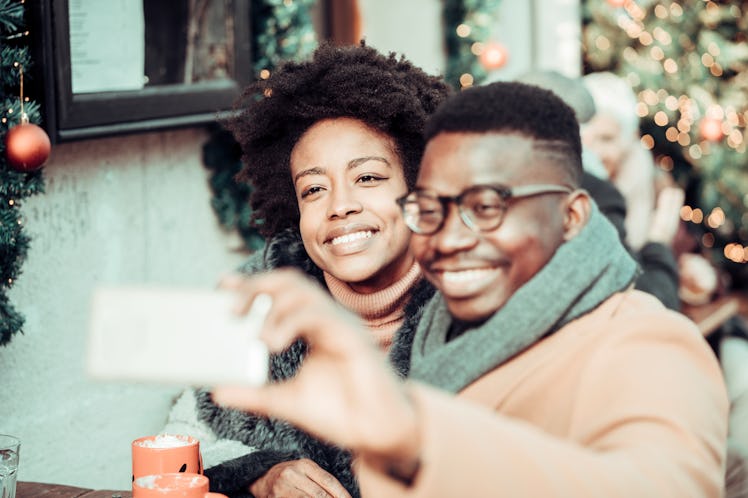 A young Black couple has a photo shoot on a snow day with holiday decorations and drinks.