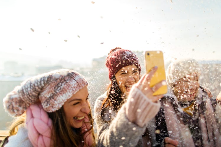 A group of women laugh while filming a snow day TikTok on a rooftop at golden hour.