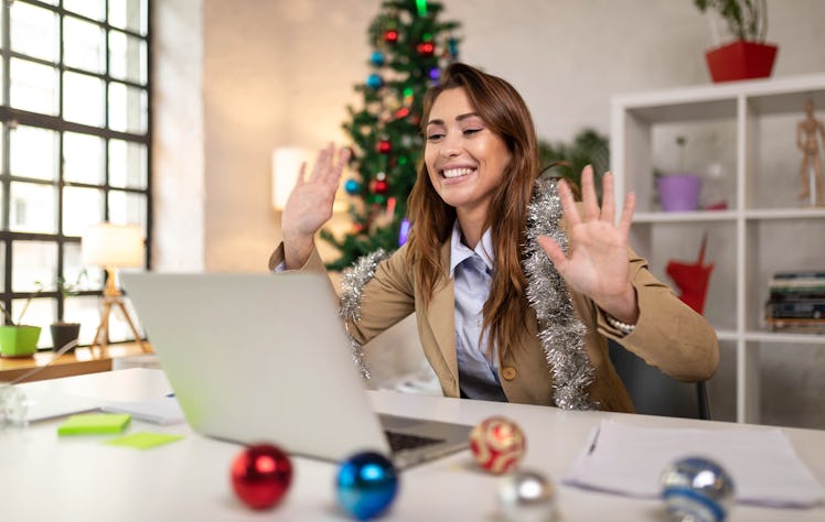 A happy woman dressed in work attire smiles at her laptop while on a virtual holiday work party.