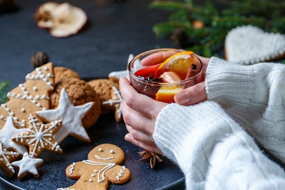 A woman holds a Christmas cocktail next to gingerbread cookies.
