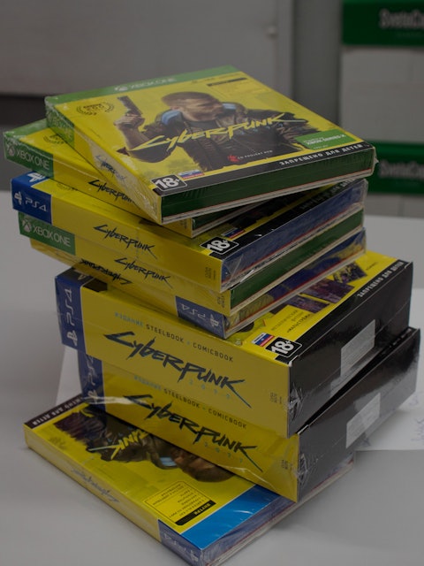 Physical copies of the game 'Cyberpunk 2077' stacked on a table. 