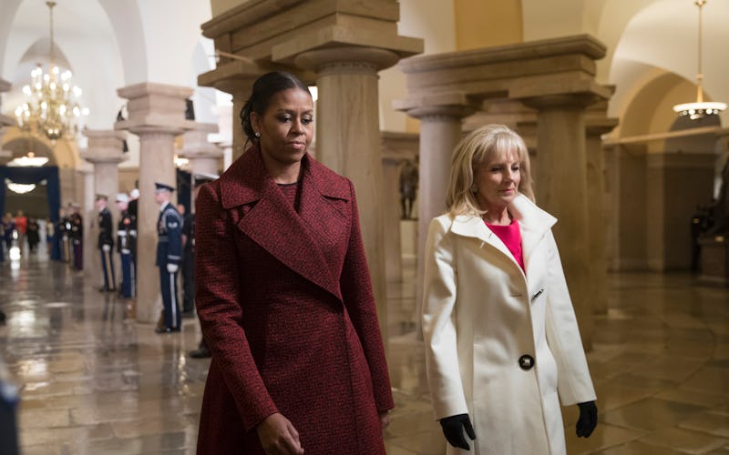 Michelle Obama and Jill biden walking down a grand hall in red and white coats