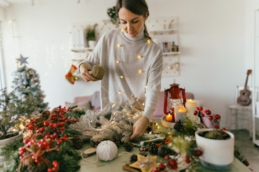 A woman wrapped in fairy lights crafts at her table to make Christmas ornaments for a merry artmas h...