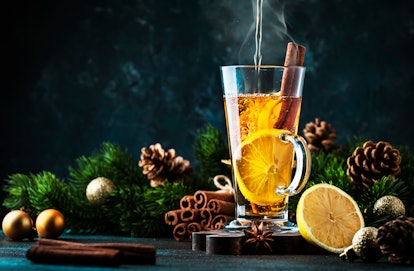 Hot water is poured into a hot toddy glass with lemon slices and a cinnamon stick, while sitting nex...