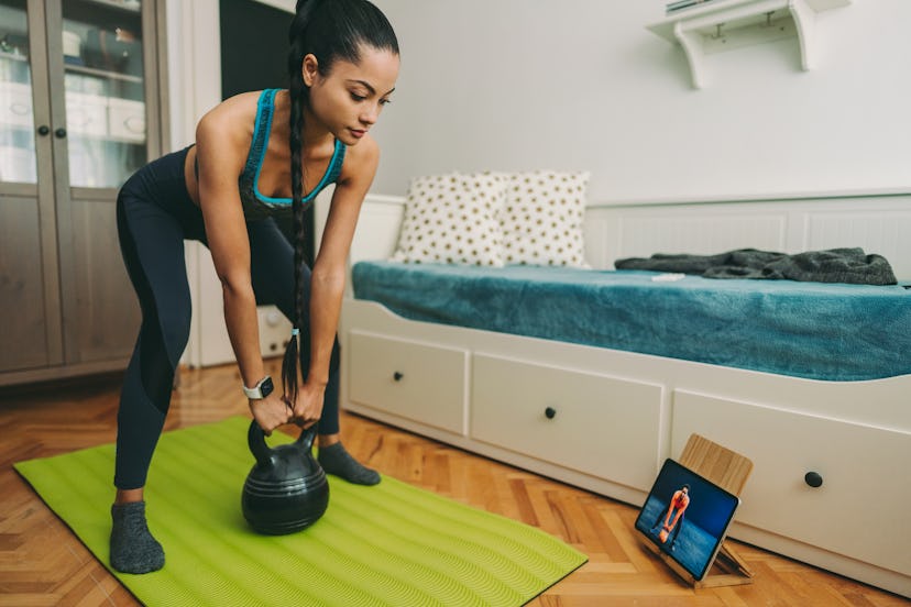 A woman does a kettlebell routine virtual workout at home. A ClassPass report reveals the most popul...