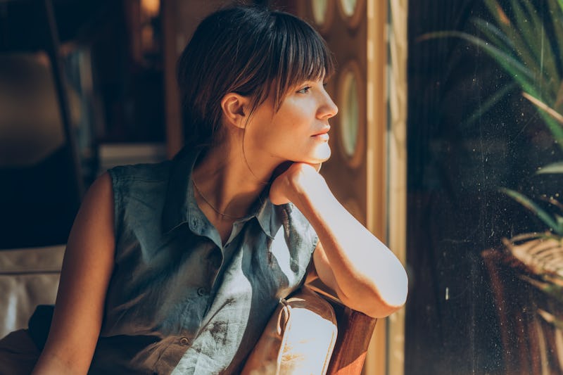 A woman stares out the window near a plant. Maladaptive daydreaming is all over TikTok's for you pag...