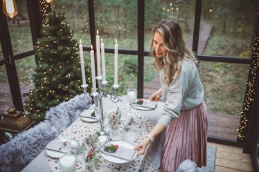 A trendy woman sets a Christmas dinner table in a greenhouse.