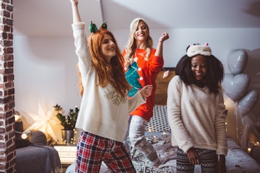 Three friends in Christmas pajamas dance around their bedroom. 