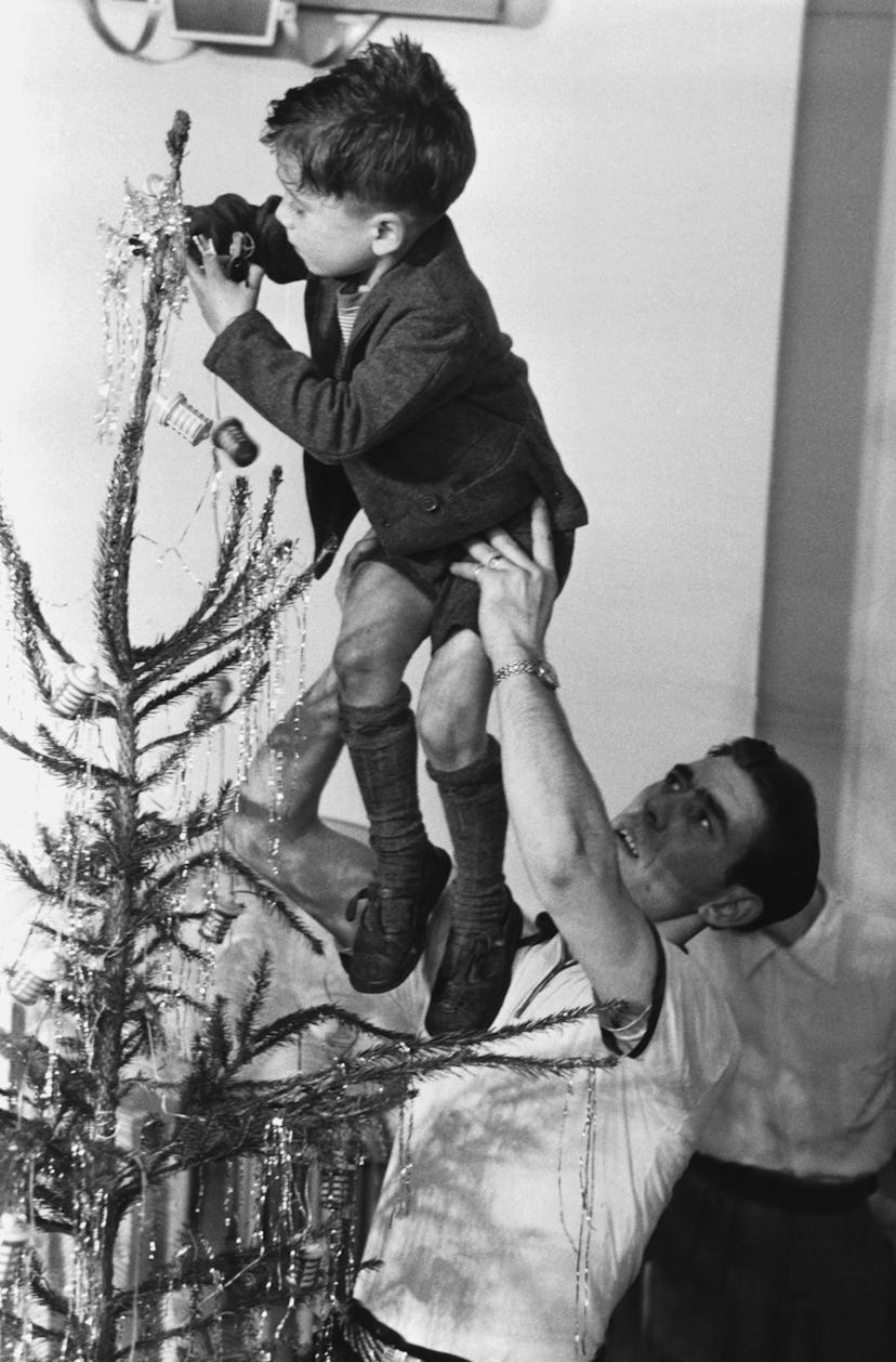 This vintage Christmas photo shows a man lifting up a boy to decorate their tree.