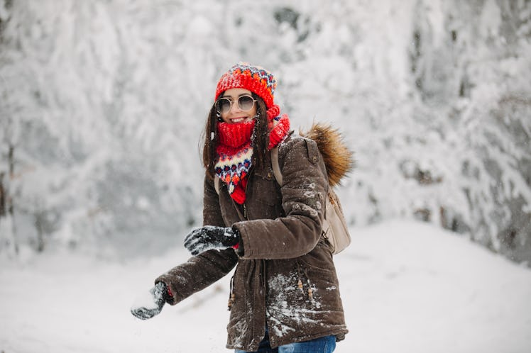 A happy woman bundled up for winter grabs snow to throw.