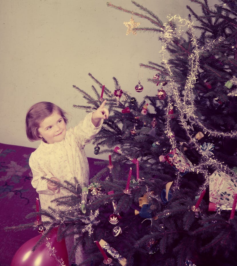 This vintage Christmas photo shows a girl pointing to a decorated tree.