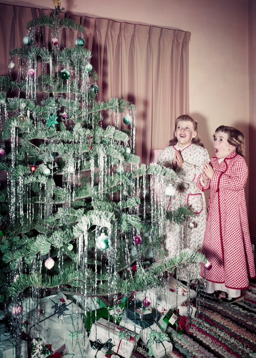 This vintage Christmas photo shows two girls in the 1950s admiring their tree. 