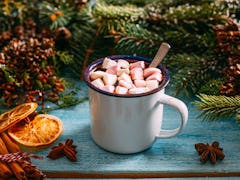 A hot chocolate sits on a table next to holiday table decor like cinnamon sticks and garland. 