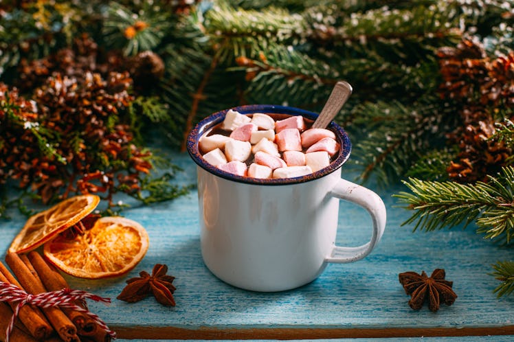 A hot chocolate sits on a table next to holiday table decor like cinnamon sticks and garland. 