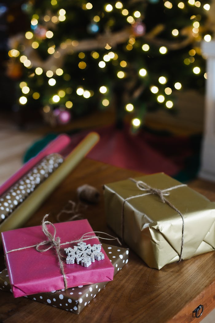 Wrapped presents next to unused wrapping paper with a decorated christmas tree in the background