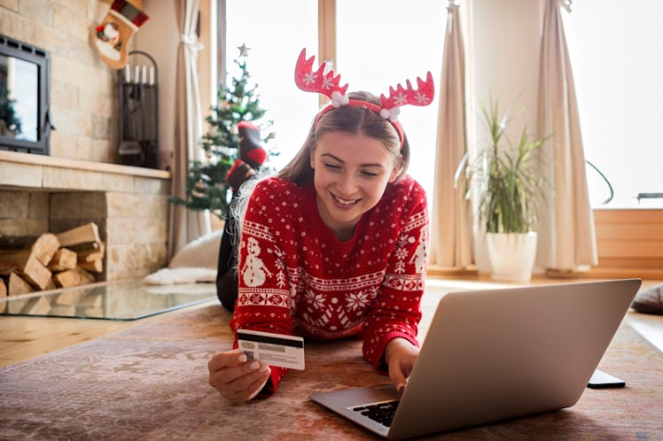 A happy woman dressed in a red and white Christmas sweater and an antler headband looks at her credi...