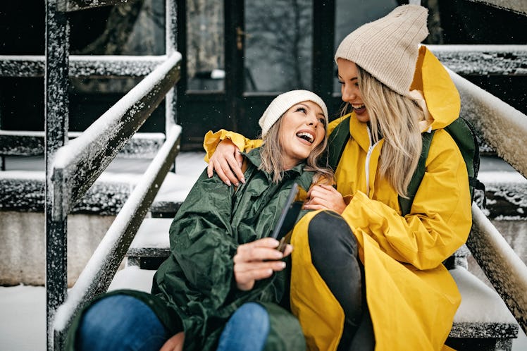A happy couple laughs while sitting on the snowy steps of a winter cabin, for which they'll need win...