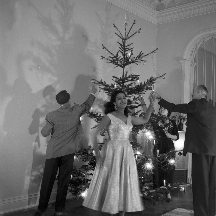 This vintage Christmas photo from 1955 shows people dancing in front of a tree.
