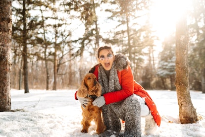 A happy woman in a red winter coat poses with her dog in the snow.