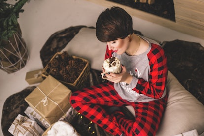 A happy woman in Christmas pjs sips a hot chocolate next to presents.