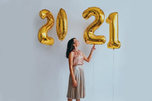 A woman wearing a pink and grey dress standing next to 4 balloons that present the year of 2021