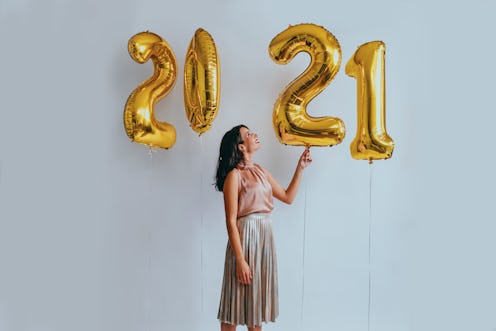 A woman wearing a pink and grey dress standing next to 4 balloons that present the year of 2021