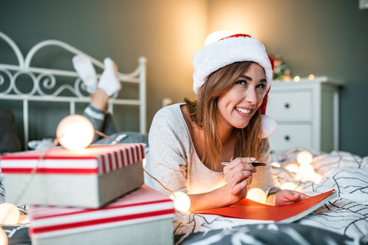 A happy woman writes out a Christmas card on her bed.