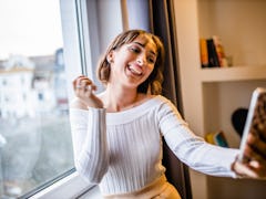 A glowing woman takes a selfie in front of a window.