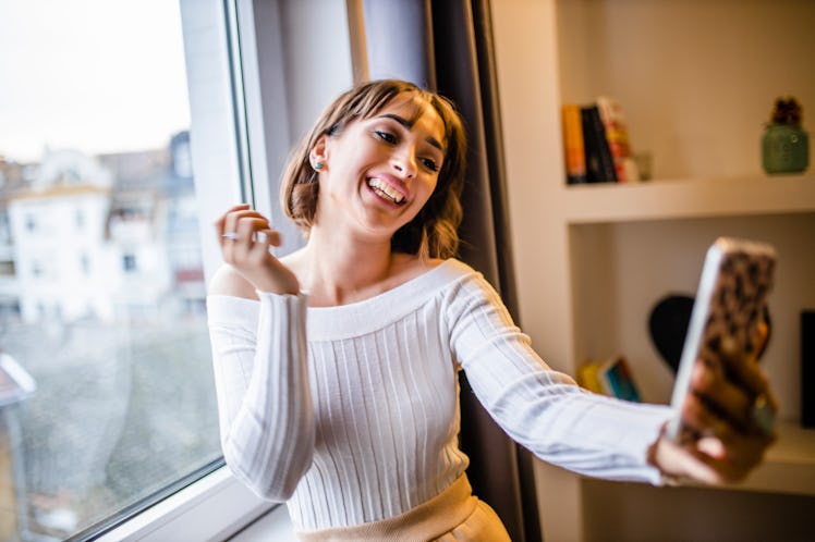 A glowing woman takes a selfie in front of a window.