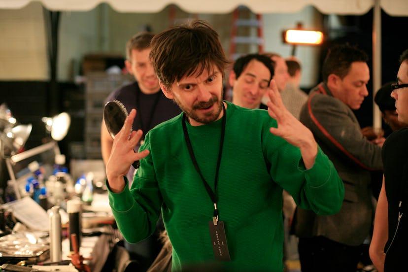 Hairstylist Guido Palau in a green sweater explaining something with a group of people standing behi...