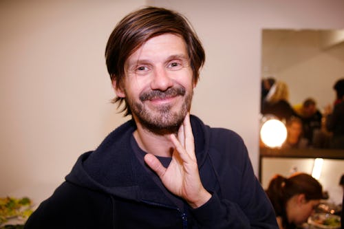Hairstylist Guido Palau smiling in a navy shirt with his hand leaned on his chin