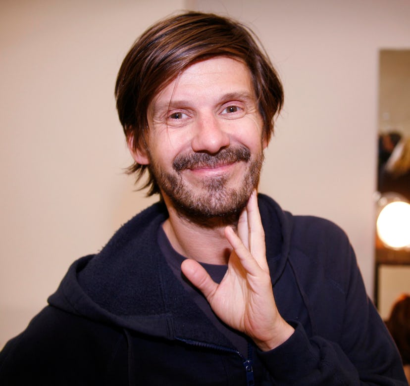 Hairstylist Guido Palau smiling in a navy shirt with his hand leaned on his chin