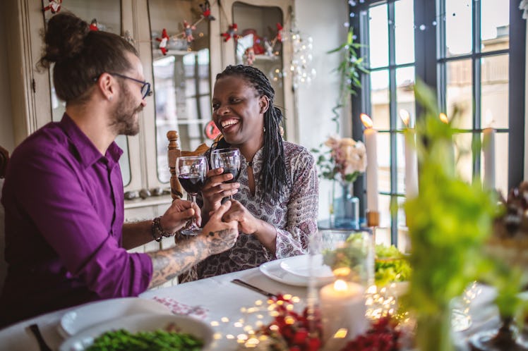 A happy couple clinks their wine glasses while enjoying a romantic and festive dinner at home.