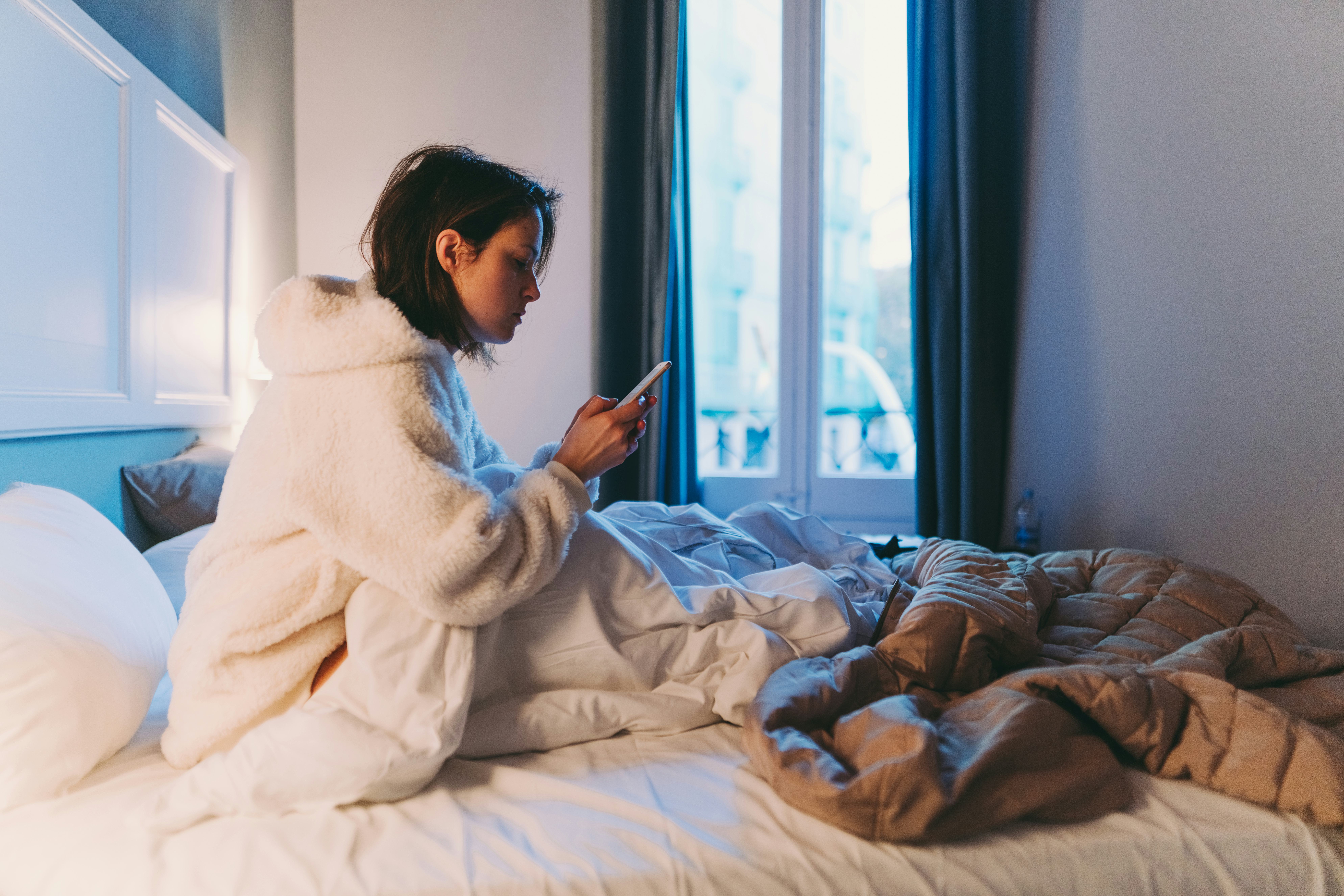 A woman checks her phone while in bed with COVID.