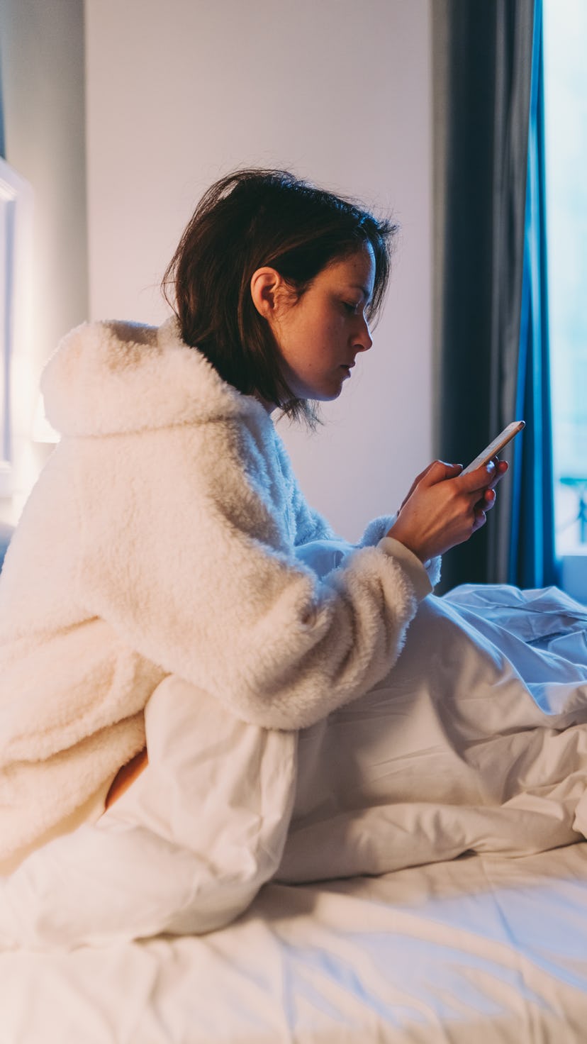 A woman checks her phone while in bed with COVID.