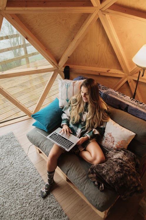 A woman in a yurt works on a laptop. These holiday 2020 staycation ideas will scratch your travel it...